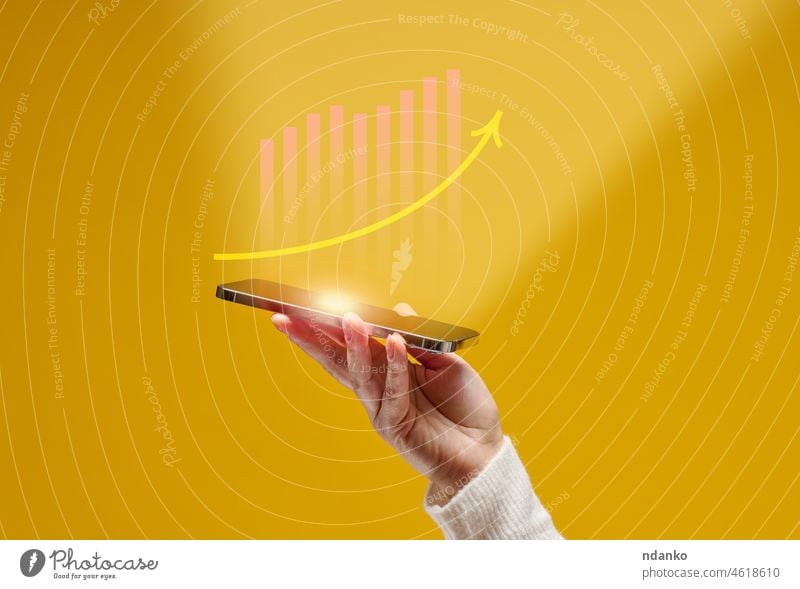 female hand holds a smartphone with holographic graphics on a yellow background. Performance growth, success internet analysis analyzing arm arrow benefit