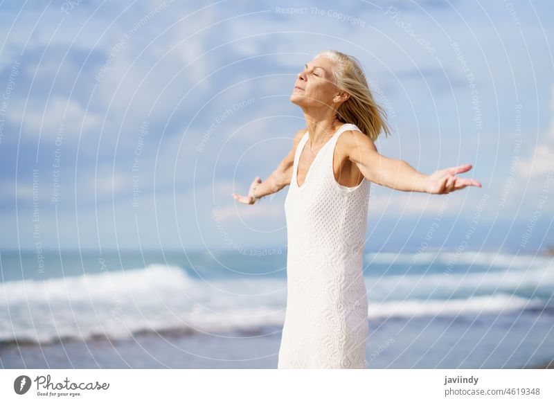 Mature woman breathing the beach air with her eyes closed and her arms open. mature senior old person elderly retirement female lifestyle happy sea holiday