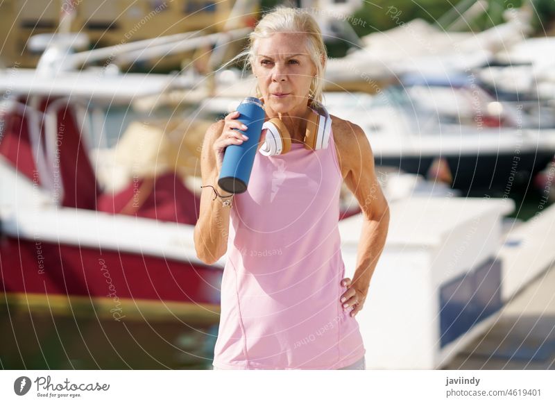 Senior woman in fitness clothing drinking water from a metal fitness bottle outdoors. mature resting senior active workout runner healthy person female