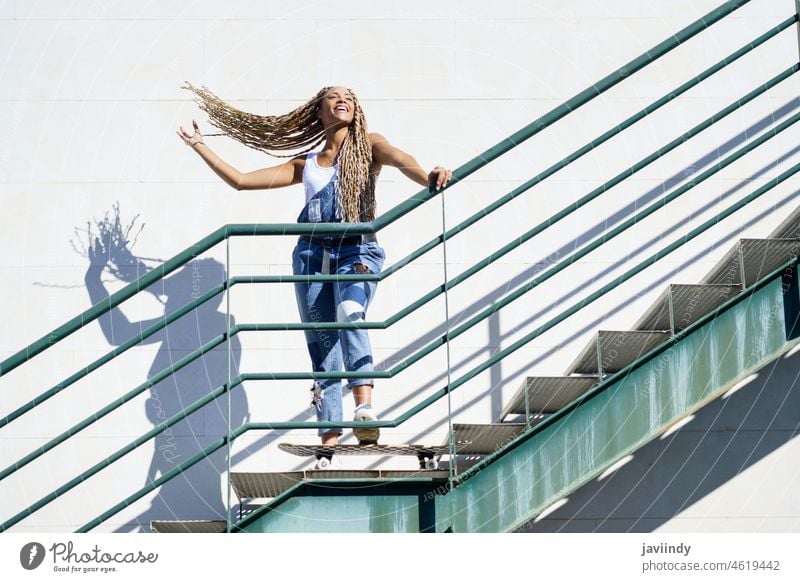 Black girl on an urban staircase, moving her coloured braids in the wind. Typical African hairstyle. woman black afrobraid dreadlocks african skateboard young