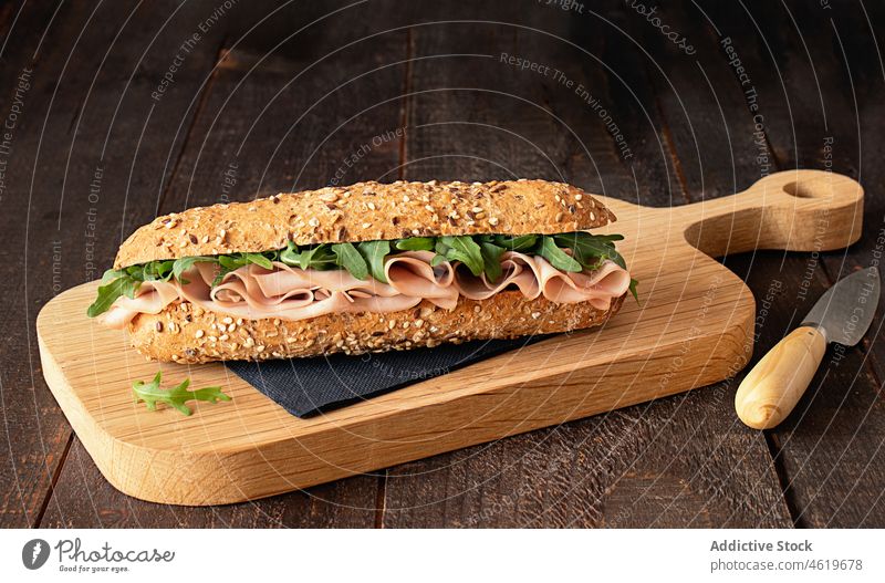 Ham sandwich with rocket leaves on wooden cutting board mediterranean mortadella baguette french bread meal food delicious rustic paper napkin panini snack ham