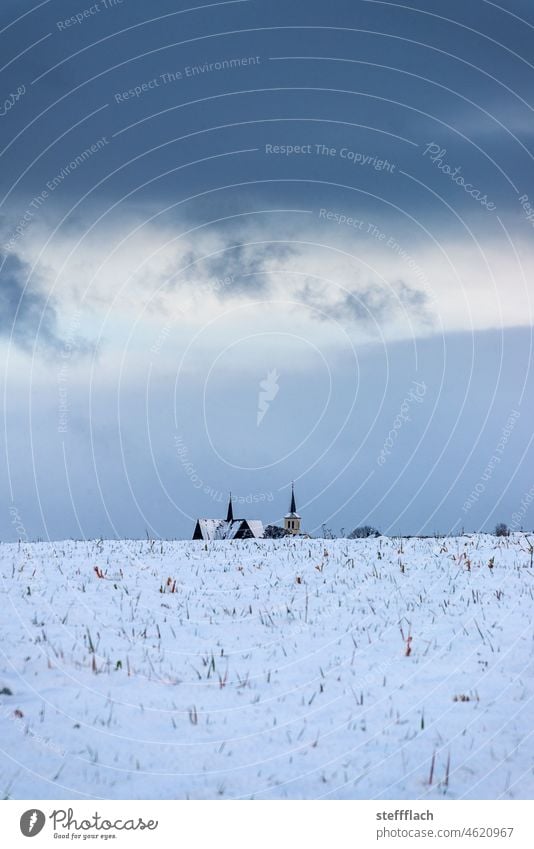 Two churches behind snow covered fields against dark cloudy winter sky Clouds Dark somber Cold Sky Blue dark blue Gray Winter Twilight Evening Sunset stormy