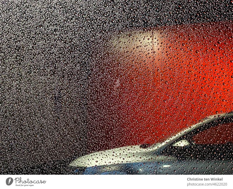 View through a rainy car window, next door a silver car parked in front of a red illuminated wall Rainy weather raindrops Car Window red wall Parking Light