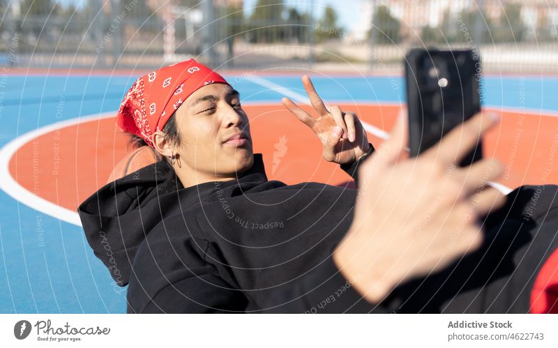 Asian man taking selfie on plauground smartphone self portrait v sign playground sports ground hobby training asian fence male activity player sportsman