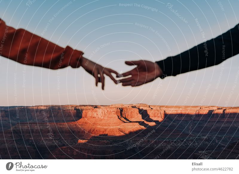 A couple reaches for each others hands in front of canyon in the desert couples reaching reaching out canyons western sunrise love support landscape western usa