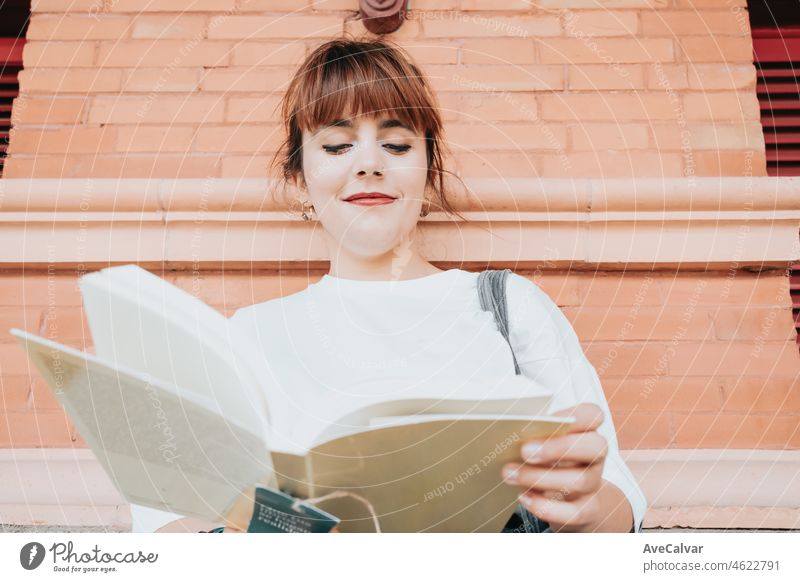 Young woman on white shirt holding and reading a book at the train station, reading everywhere people, book hobby fan. Waiting for the train to come, killing free time activities and habits