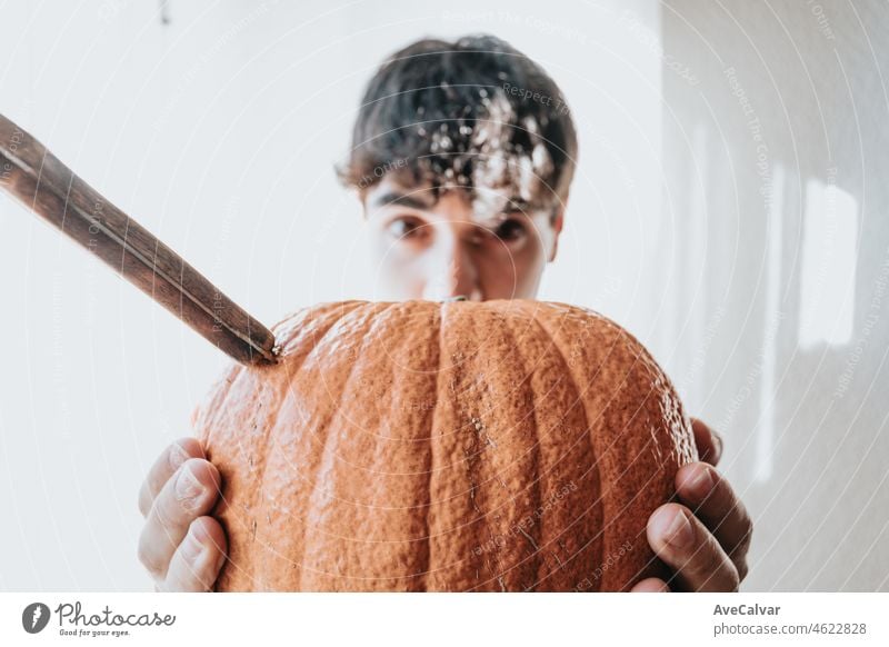 Young man holding on his hands a super textured pumpkin with a knife getting ready for halloween. Work and manual activities at home, party at home concept. Close up image funny happy image