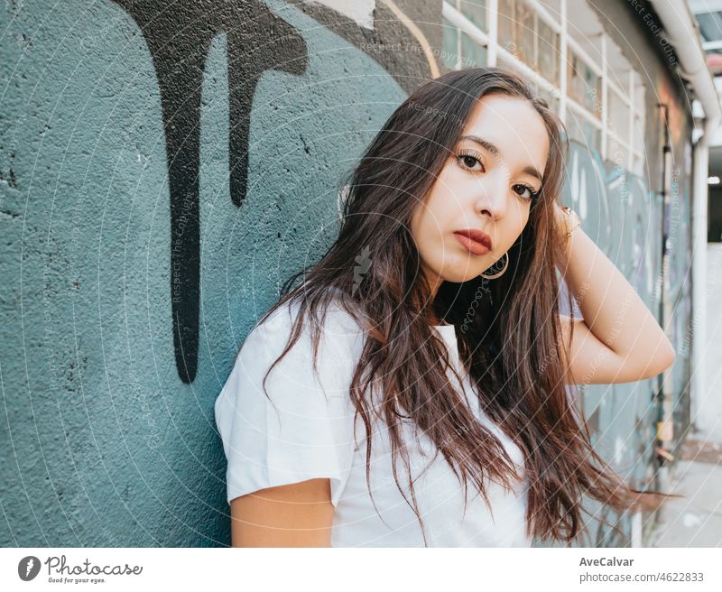 Portrait of a young arab african girl on serious hip hop youngster attitude looking serious to camera on a white shirt with a graffiti background. Beauty young street life street artist at the city