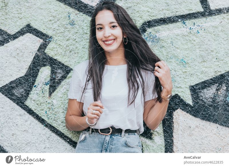 Portrait of a young arab african girl on smiling hip hop youngster attitude looking serious to camera on a white shirt with a graffiti background. Social network model concept, photo like share social