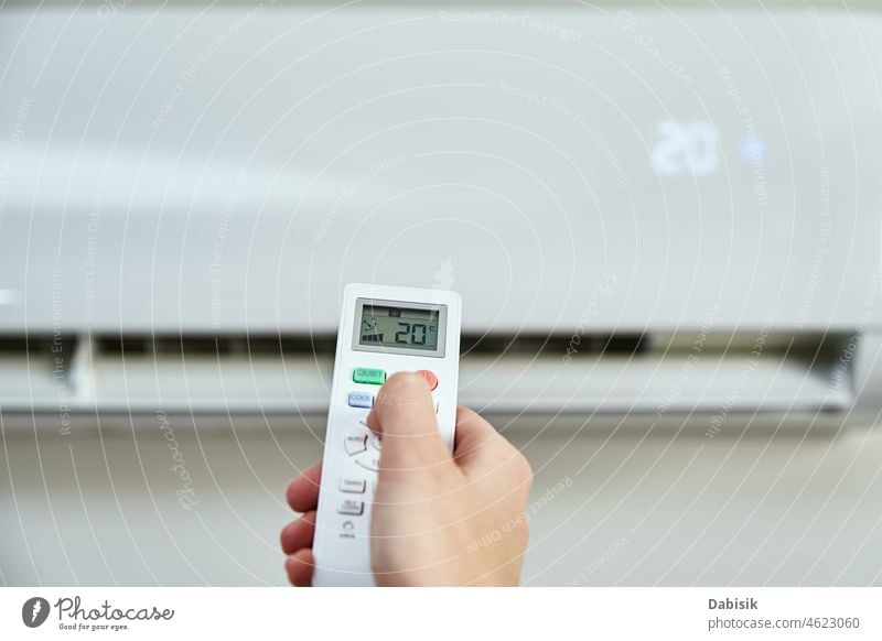 Hand adjusting temperature on air conditioner remote control home turn on heat cold comfortable climate appliance activate turn off summer blade hot blow