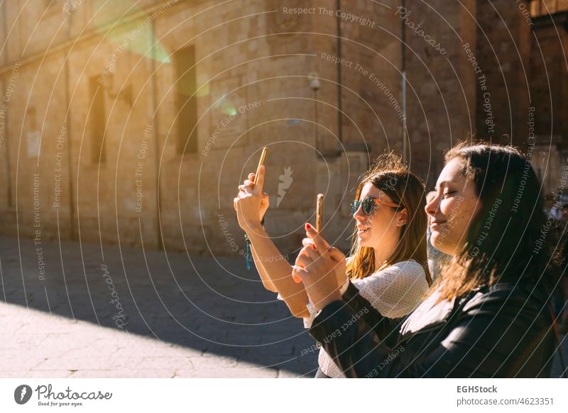 Two women tourist visiting an ancient city in spain taking a picture of a Salamanca monument with her mobile phone at sunset two friends vacation holidays
