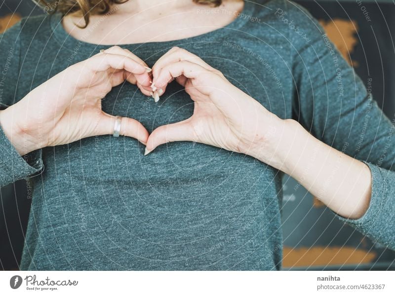 Young woman making a heart sign with her hands solidarity humanity help concept conceptual chest white real people human beign good gray map simple life