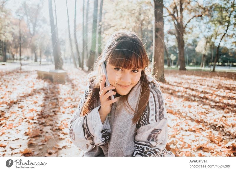 Young woman having a fun call during a sunset at the forest during an autumnal winter day. Connectivity and social concept.Young people life style. Greeting friends online. Copy space.