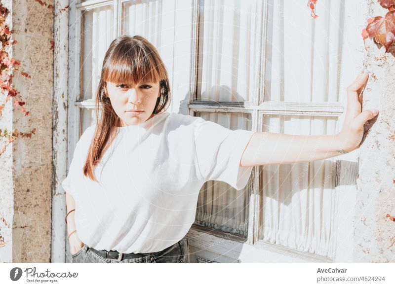 Portrait of a young redhead woman over an old white window on cool attitude, serious and confident woman, the future is woman. White shirt and modern wearing with copy space, social network concept.