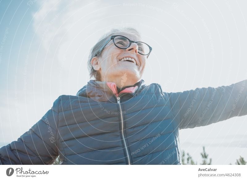 Close up portrait of a super happy smiling old woman during a walk, doing exercise and activities during the third age. Waving arms with happiness. Health care for seniors and nature sport grandma