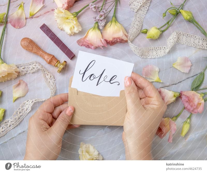 Hands with Card LOVE inside envelope near by pink flowers on a marble table hands card handwritten marry me always proposal marriage Flowers top view Marble