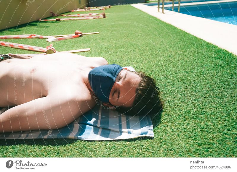 Young man in a swimming pool at summer wearing a face mask covid pandemic covid-19 male holidays summertime contagious risk protection influenza green grass