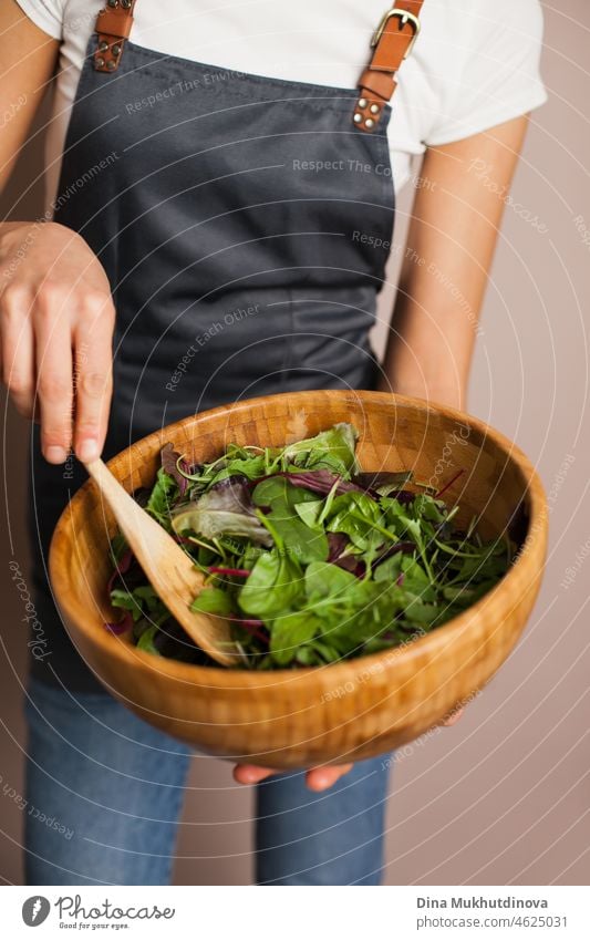 Woman chef in a gray apron making green salad in eco wooden bamboo bowl in the kitchen. Healthy eating and nutrition, eco conscious lifestyle. vegetable hand