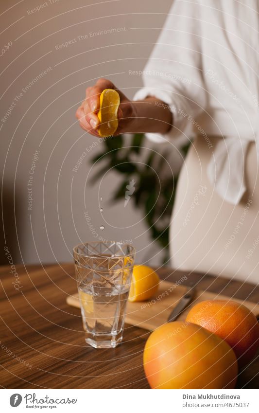 woman squeezing lemon juice into a glass of water  in the kitchen at home - healthy eating and lifestyle mineral freshness diet modern morning utensil care