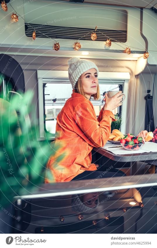 Woman having breakfast in a camper van motorhome woman thoughtful holding cup coffee morning bun looking aside beautiful pretty pensive eating healthy blueberry
