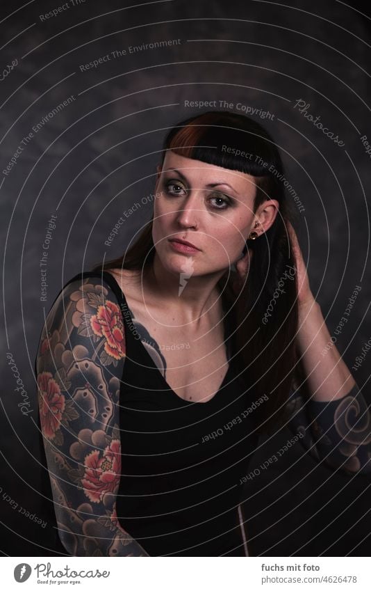 Portrait of woman on dark background Looking into the camera Tattoo tattooed girl Feminine Colour photo portrait Young woman Piercing pretty Authentic