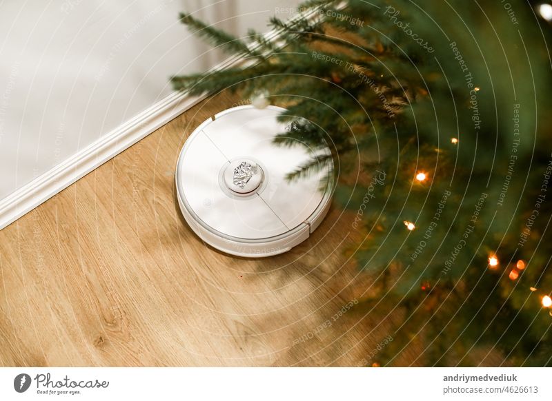 Smart home. Robot vacuum cleaner performs automatic cleaning. Cleans the parquet from Christmas tree needles after the new year. cleans near the Christmas tree after the holidays.