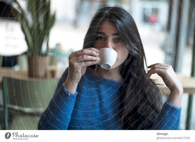 Young model look woman with long black hair is sitting in a coffee shop during the brunch brunette customer holding coffee cup freelancer hipster restaurant