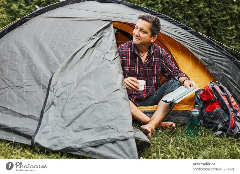 Man relaxing in tent at camping during summer vacation. Man holding map while planning next trip adventure campsite traveling active recreation equipment