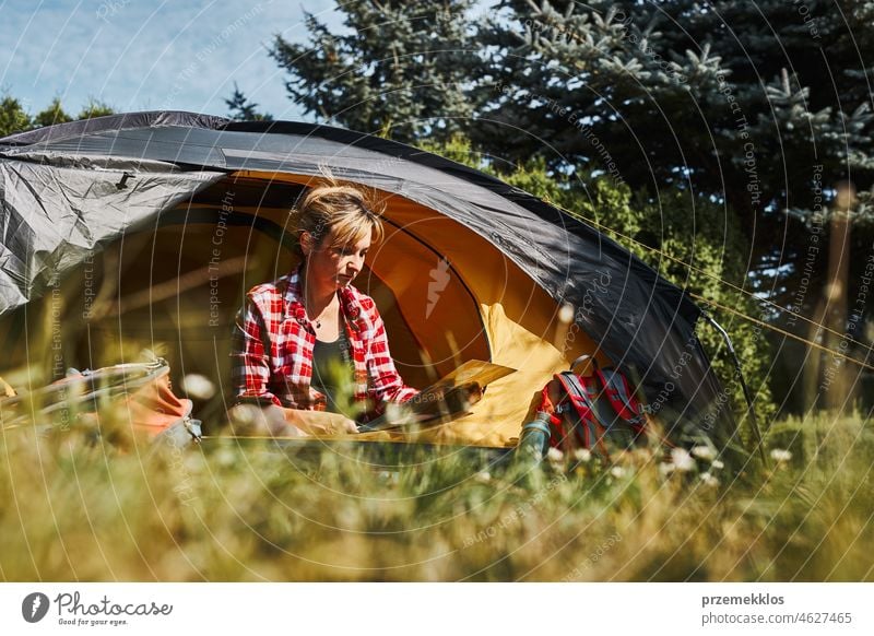 Woman planning next trip while sitting with map in tent. Woman relaxing in tent at camping during summer vacation adventure campsite traveling active recreation