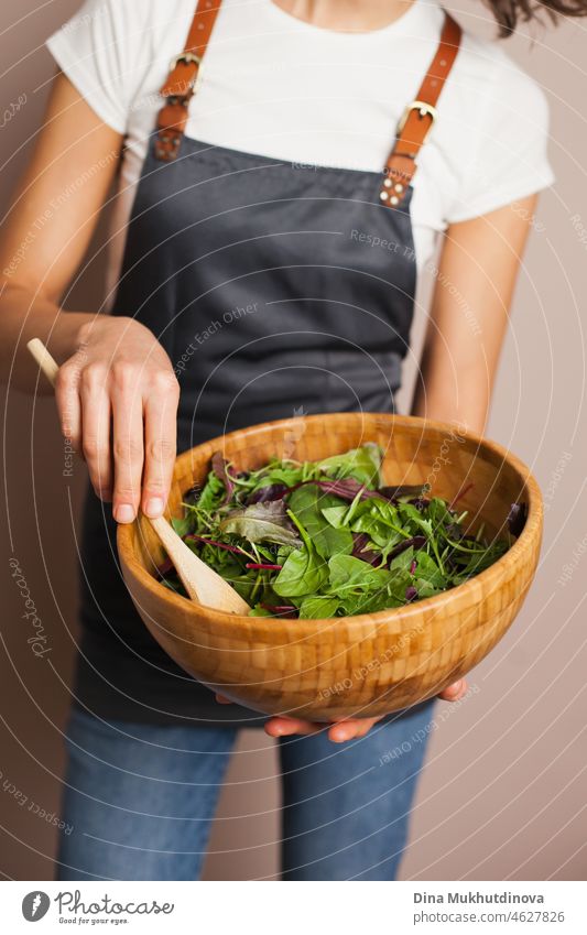 Woman in a gray apron mixing green salad in eco wooden bamboo bowl in the kitchen. Healthy eating and nutrition, eco conscious lifestyle. food vegetable hand