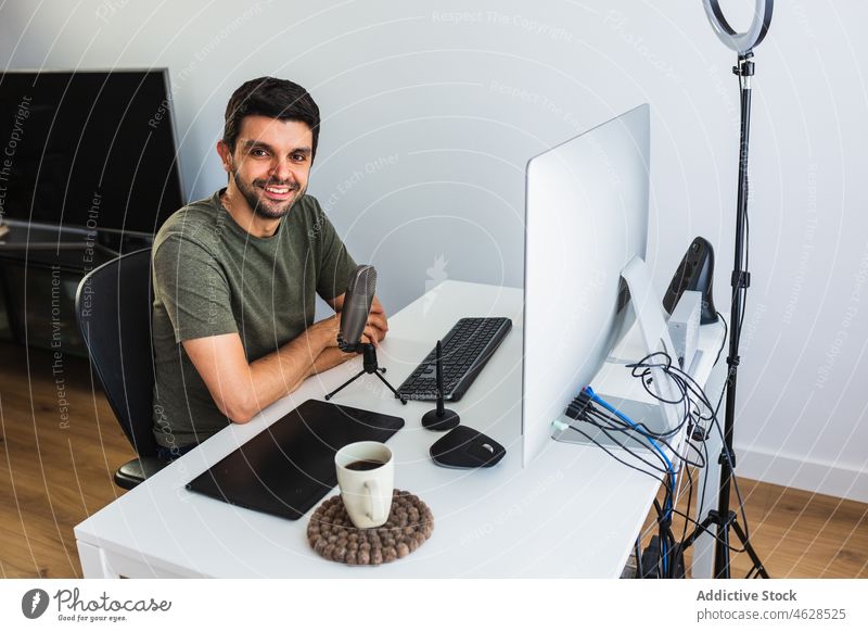 Positive designer at table with computer and microphone man online work office project workplace freelance gadget occupation device internet job desk busy