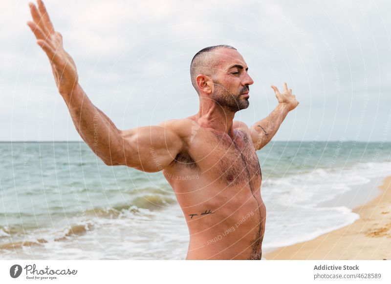 Shirtless man with spread arms on beach naked torso shirtless sea training water shore eyes closed healthy lifestyle wellbeing sporty muscular male workout