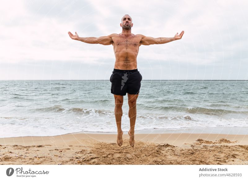 Shirtless sportsman jumping on sandy beach naked torso shirtless sea training shore healthy lifestyle exercise practice sporty wellbeing muscular male workout