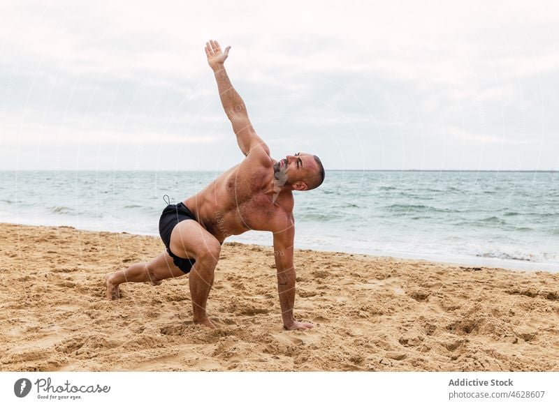 Shirtless man doing Side angle asana on beach side angle parshvakonasana yoga naked torso sea training shore healthy lifestyle exercise practice sporty