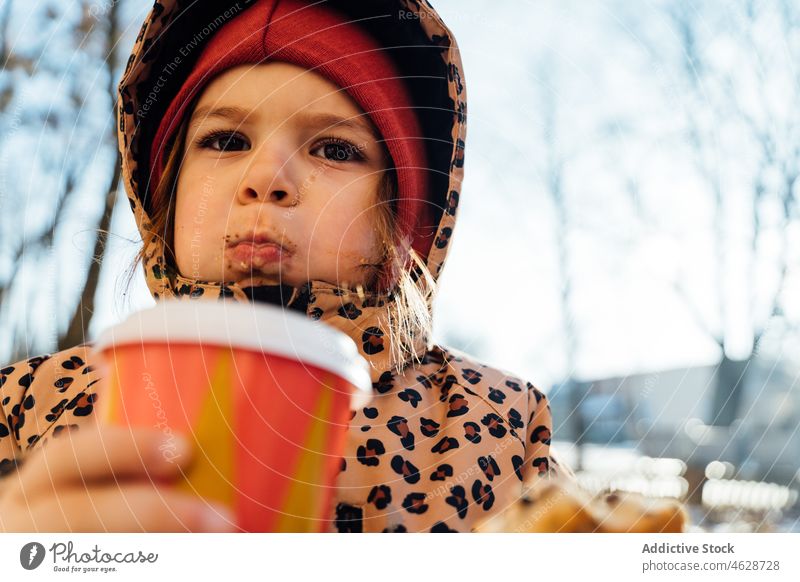 Cute girl with takeaway beverage on winter day kid cookie hot drink street city cold childhood dessert outerwear season snow coffee warm clothes serious