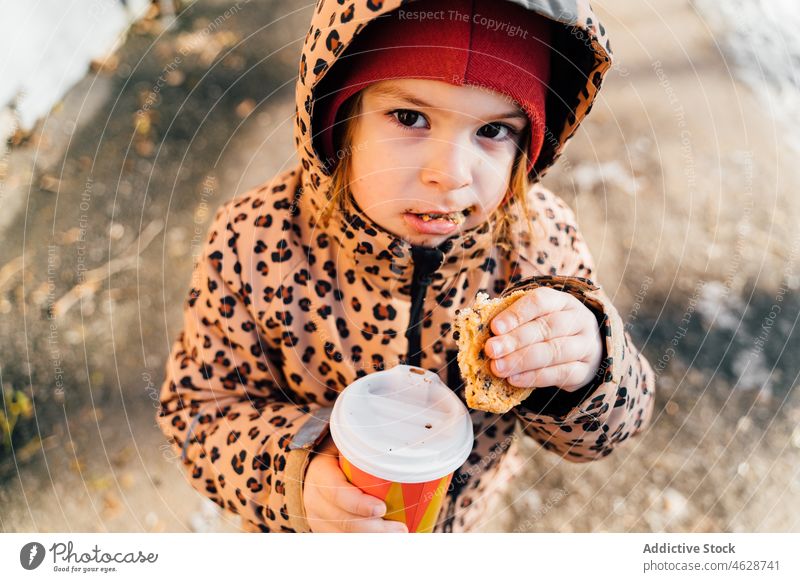 Cute girl with takeaway beverage on winter day kid cookie hot drink street city cold childhood dessert outerwear season snow coffee warm clothes paper cup