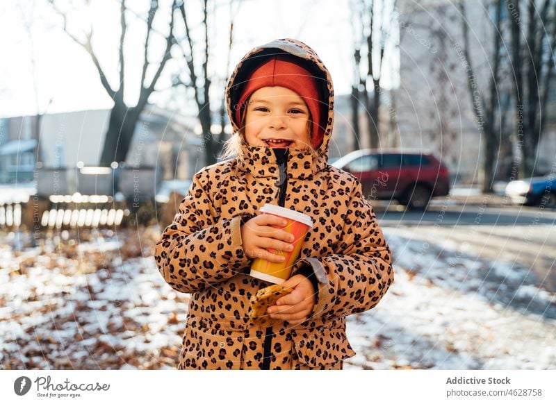 Cute girl with takeaway beverage on winter day kid cookie hot drink street city cold childhood dessert smile outerwear season cheerful snow coffee positive