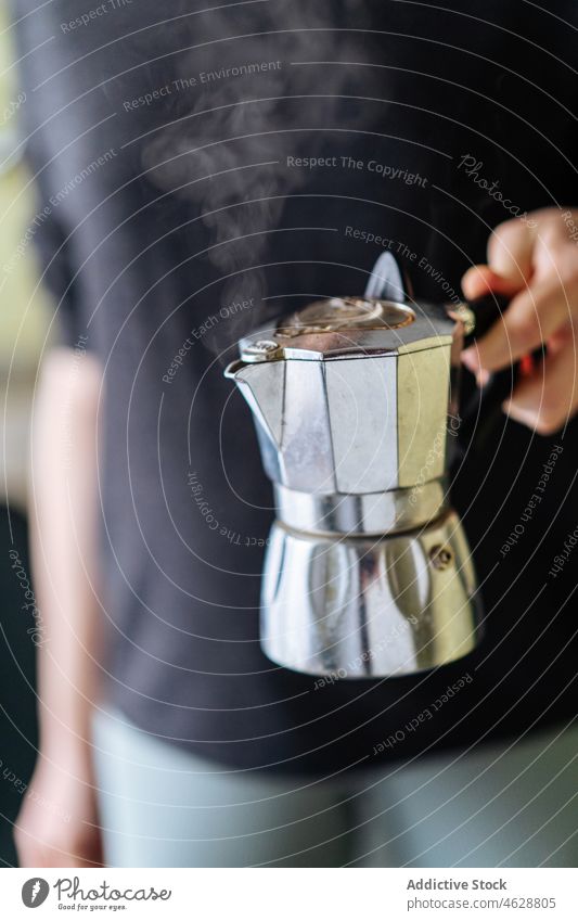 Anonymous person with moka pot coffeemaker geyser kitchen brew appliance modern hot drink equipment stainless steel metal light domestic flavor beverage style