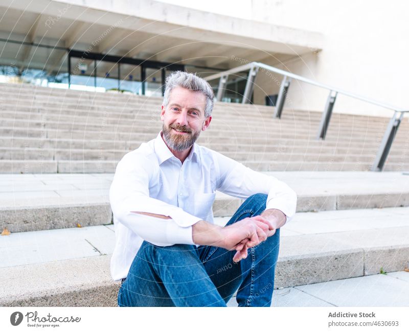 Positive businessman sitting on urban stairs entrepreneur staircase city street elegant corporate building worker male step smile beard cheerful rest stone