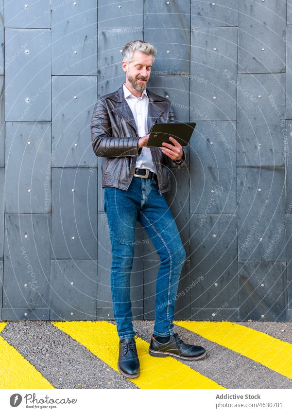 Trendy man browsing tablet near wall street online modern city connection chat internet male beard style unshaven town device gadget contemporary trendy surfing