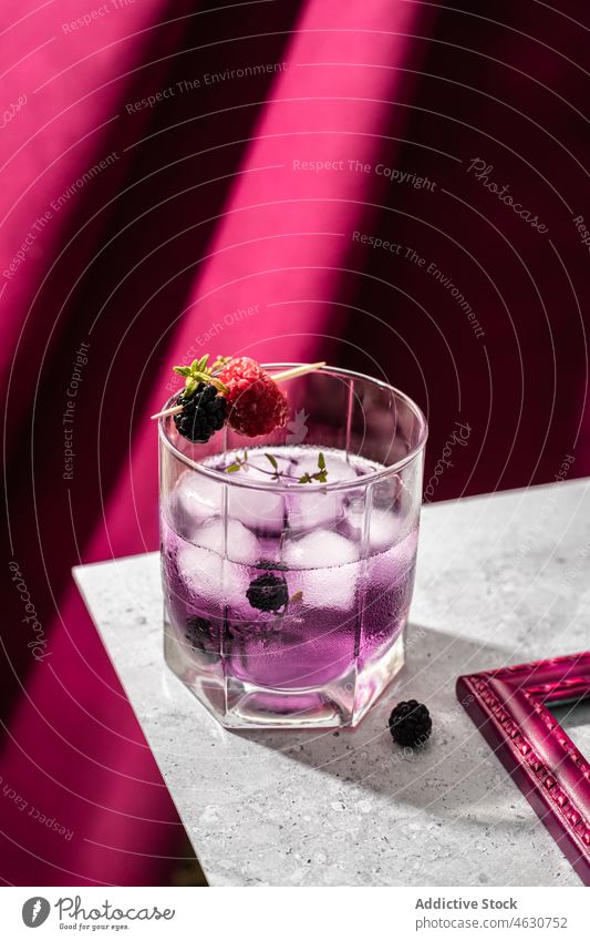Glass of blackberry cocktail with ice cubes purple refreshment raspberry glass crystal beverage aperitif cold toothpick table liquid wooden cool booze portion