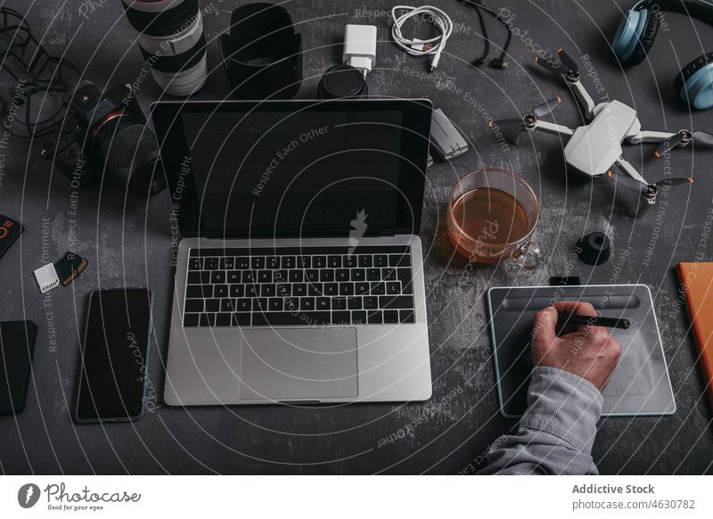 Man working on graphic tablet at workplace with different equipment man photographer using laptop stylus drone desk male smartphone tea headphones connection