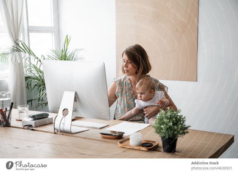 Woman with baby browsing computer mother motherhood babyhood freelance work remote workplace home occupation female job paper busy table self employed modern