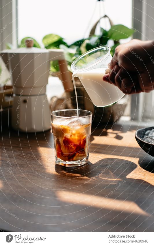 Anonymous person pouring milk into a glass with coffee and ice cold ice cube coffee press caffeine beverage refreshment kitchen morning table home tasty