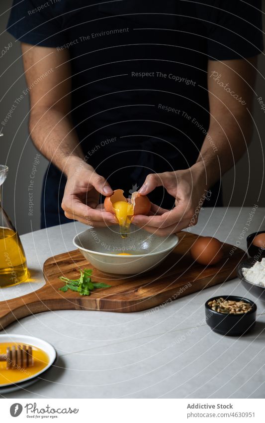 Unrecognizable man breaking egg into bowl cook culinary cuisine recipe ingredient kitchen raw chef prepare food cutting board various product table male add
