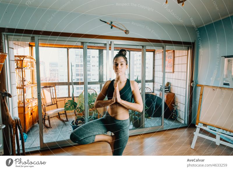 Attractive fitness young woman doing the tree Pose doing yoga with online class at home looking concentrated. Entertainment and education on the Internet. Healthy lifestyle concept during free time.