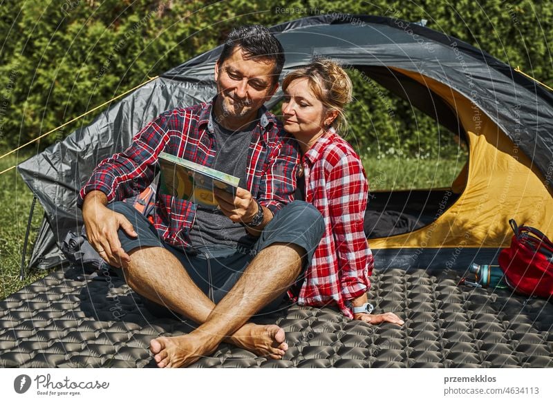 Couple planning next trip while sitting with map by tent. People relaxing at camping during summer vacation adventure campsite traveling active recreation