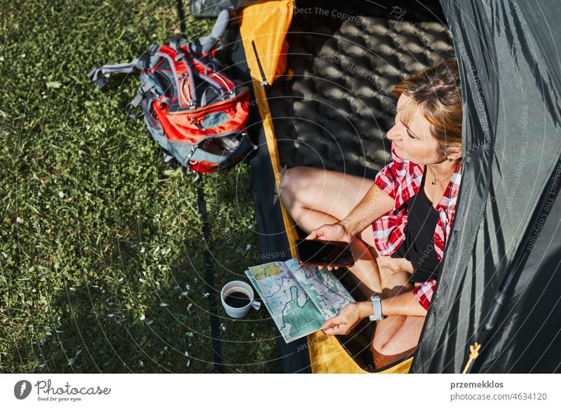 Woman planning next trip while sitting with map in tent. Woman relaxing in tent at camping during summer vacation adventure campsite traveling active recreation