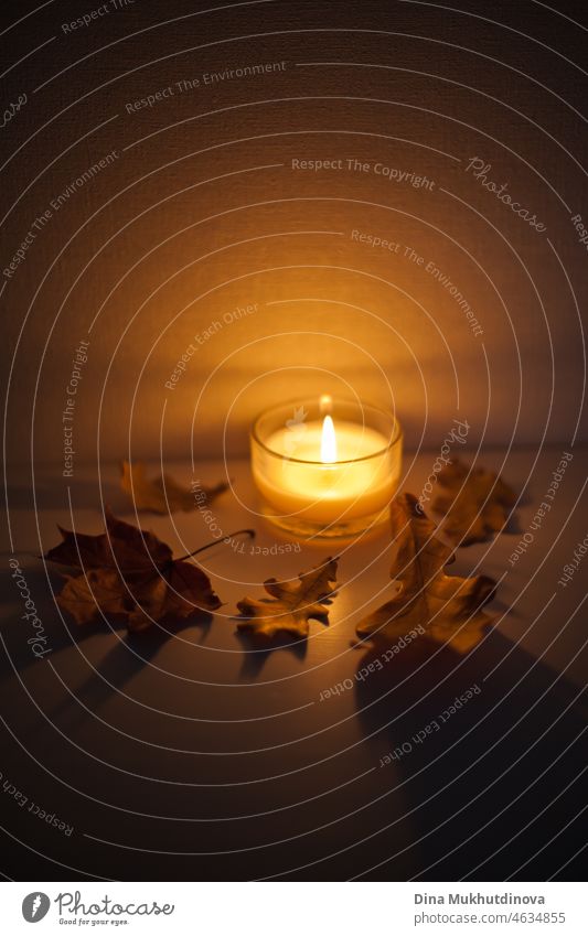 Candle glowing on the bedside table with autumn leaves around it - cozy vibes and mood at home in the evening or romantic night flame candle candlelight fire