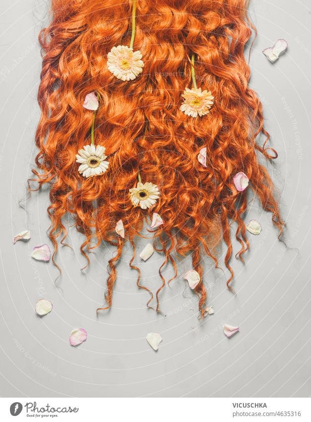 Long red curly hair with white, yellow and pink petals on pale grey background. long beauty concept flowers hairdresser top view beautiful care clean color